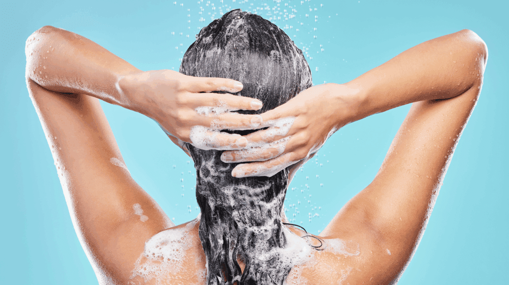 AWA Purification Technologies water filtration systems South Texas - Person washing their hair, seen from behind, with lathered shampoo covering their dark hair and hands on the back of their head. Water droplets from advanced water purification systems glisten against a blue background.