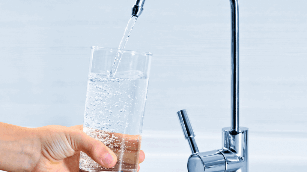 AWA Purification Technologies water filtration systems South Texas - A hand holds a clear glass under a modern kitchen faucet, filling it with fresh water—likely filtered by advanced water purification systems—bubbles visible in the water against a light background, perfect for residential and commercial settings.